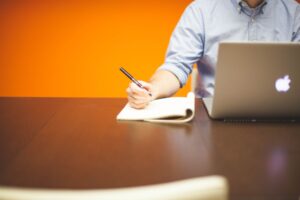 Writing article ideas in a notebook beside a laptop, planning an HVAC blog